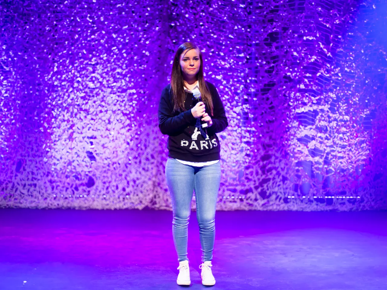 This picture shows a girl standing and she is holding a microphone in her hand and we see lighting...