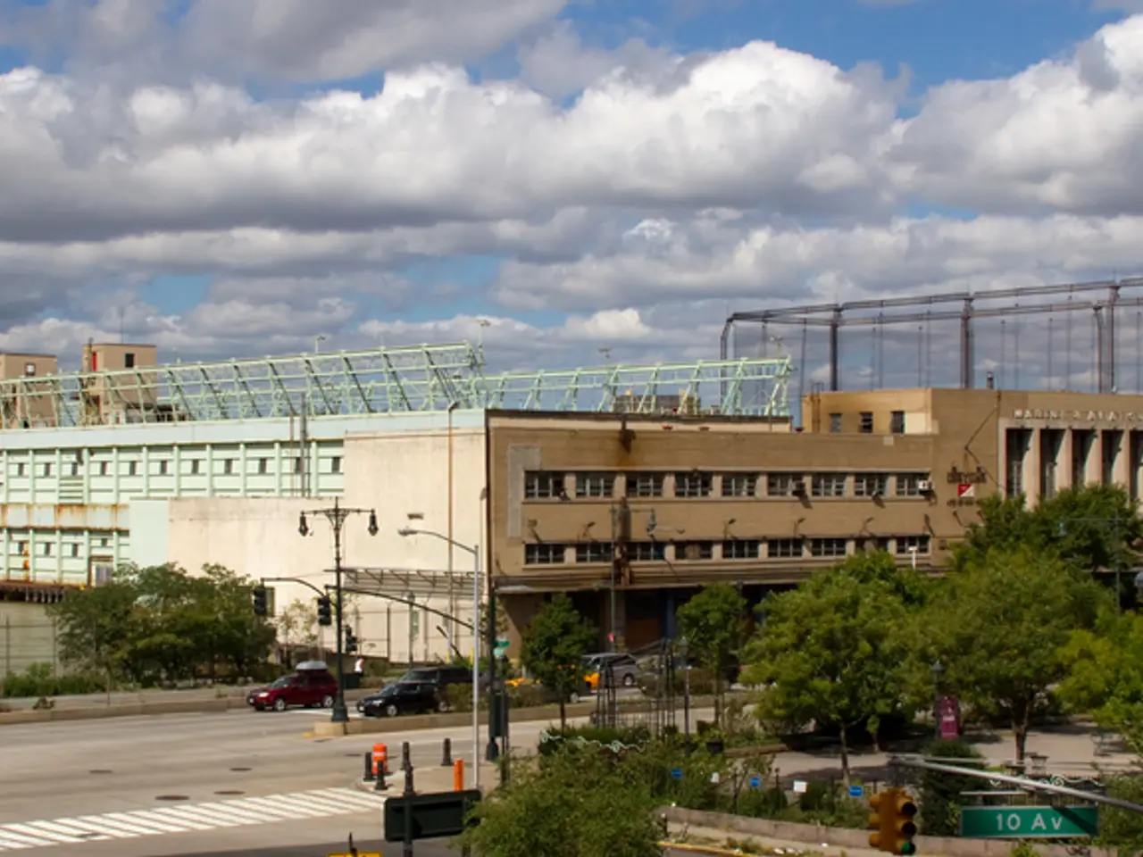 In the image there is a road, vehicles, trees, street lights, a water surface and a huge...