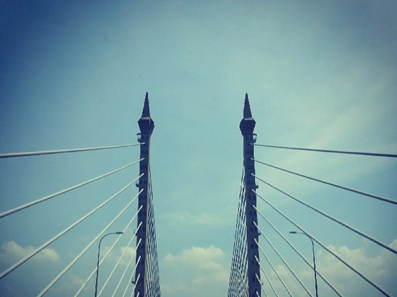 In this image, we can see poles. At the bottom, there are few vehicles on the road. Background we...