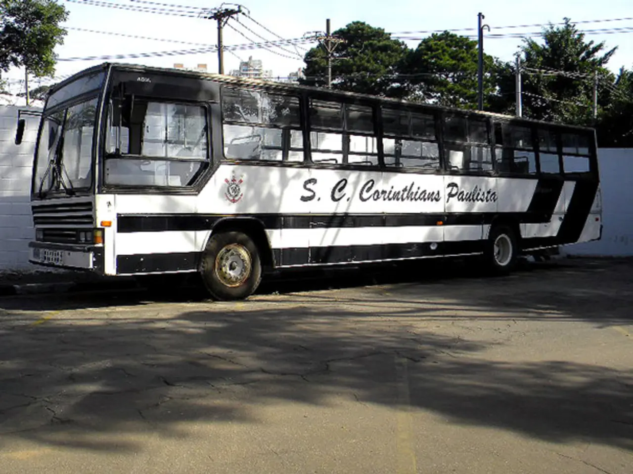 In this picture we can see a bus parked on the road and behind the road there is a wall, electric...