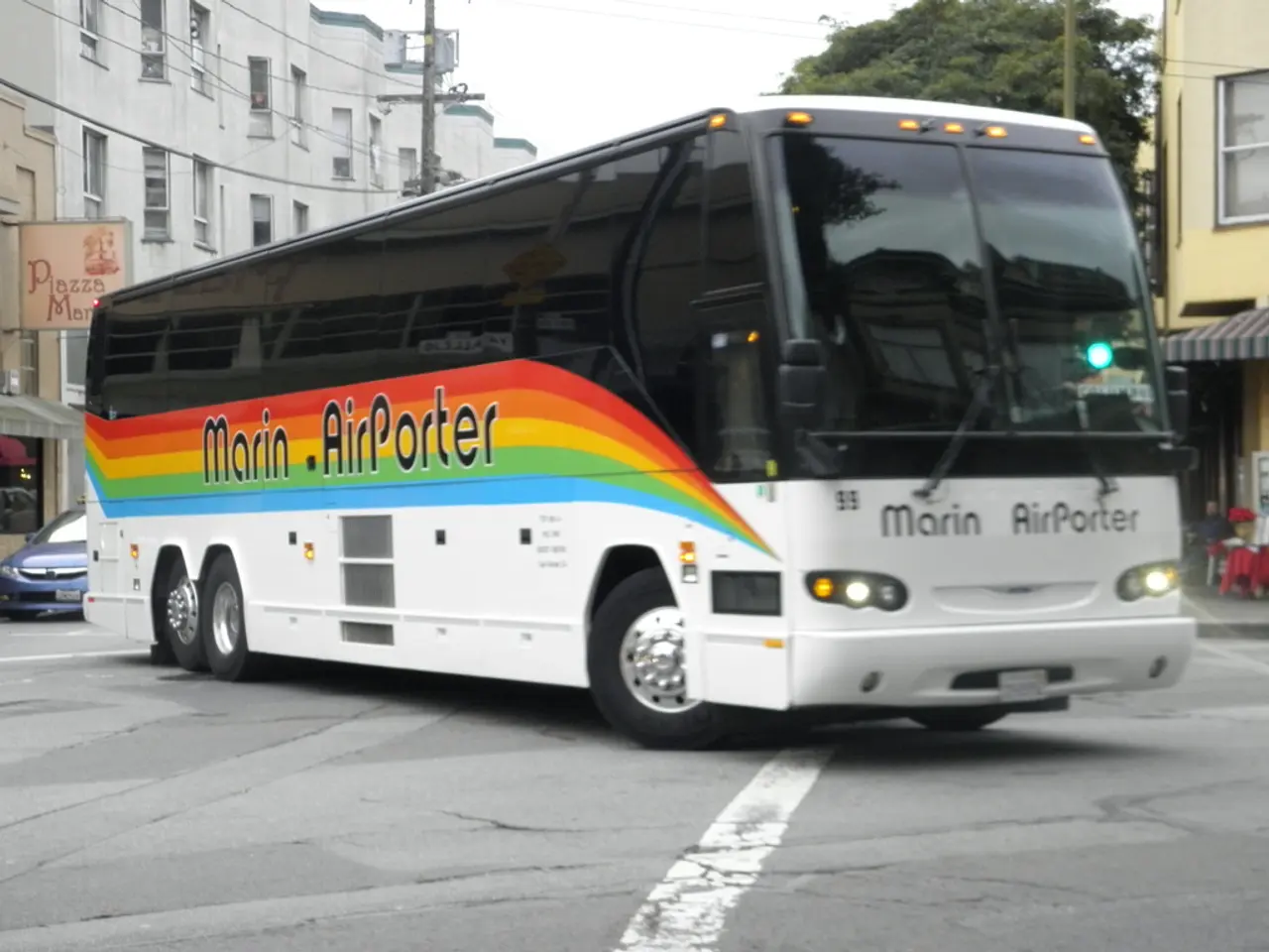 In this image there is a bus on a road, in the background there are buildings and tree and poles.