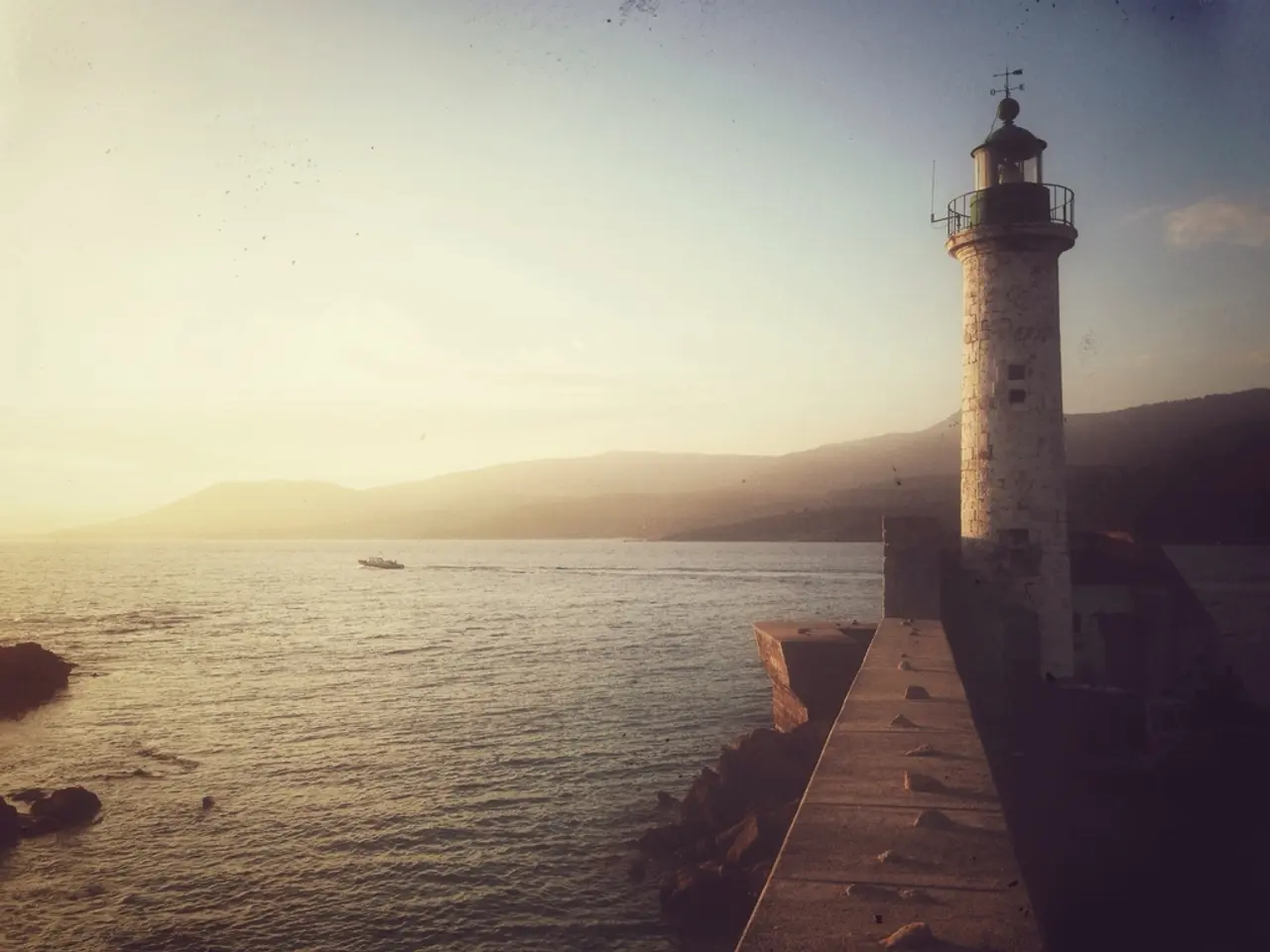 In this image we can see sea, hills, sky, lighthouse and rocks.