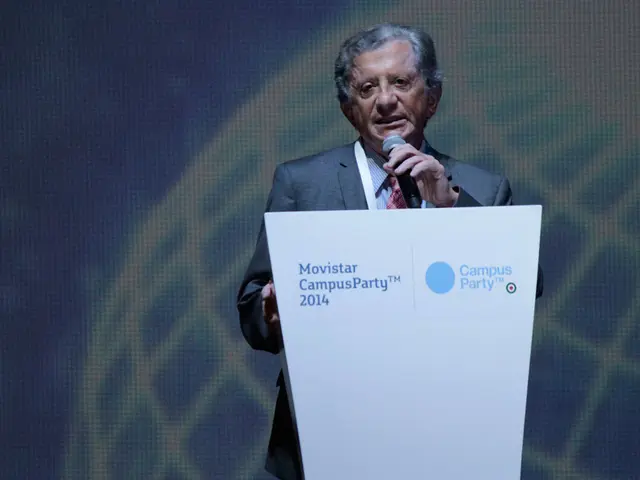 In this image we can see a person standing near the podium and speaking into a microphone. There is...