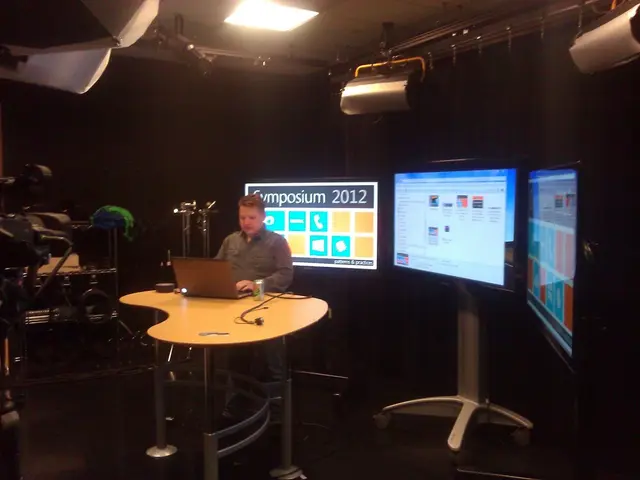 This is the picture of a man sitting in the chair and operating a laptop in the table and in back...